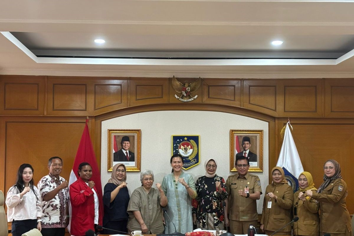 A group of men and women in formal and official attire pose with fists raised in a government meeting room with national symbols on the wall behind them