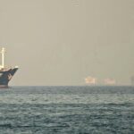 Large cargo ship azayez on calm water near a hazy harbor with another vessel in the distance daylight haze