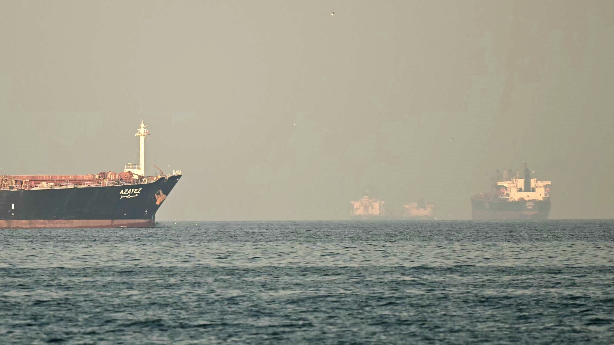 Selat hormus catrawarta Large cargo ship azayez on calm water near a hazy harbor with another vessel in the distance daylight haze