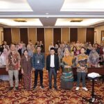 Group photo of conference attendees in a large meeting room front row standing and others behind them
