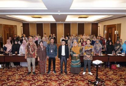 Group photo of conference attendees in a large meeting room, front row standing and others behind them