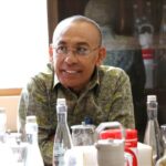 Smiling man with glasses seated at a table with water bottles and condiments in a restaurant setting
