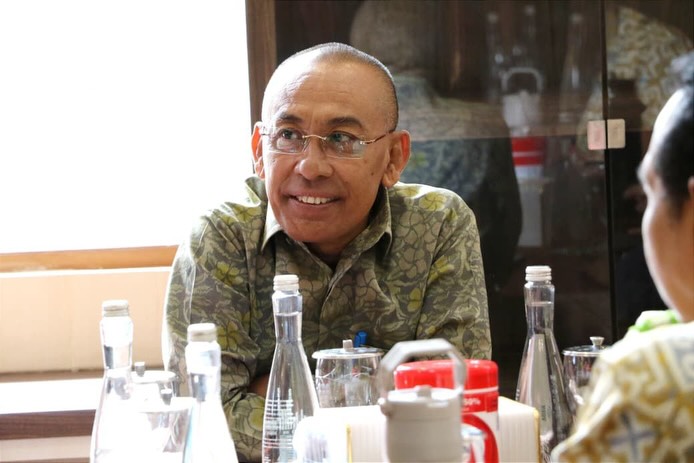 Smiling man with glasses seated at a table with water bottles and condiments in a restaurant setting.