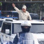Police officer stands in an open sunroof of a white suv saluting during a convoy   but lets correct syntax