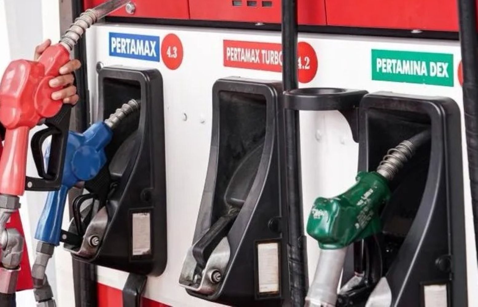 10fbbm1 catrawarta Gas pump panel with three nozzle handles red blue green at a fuel station labeled pertamax and pertamina dex