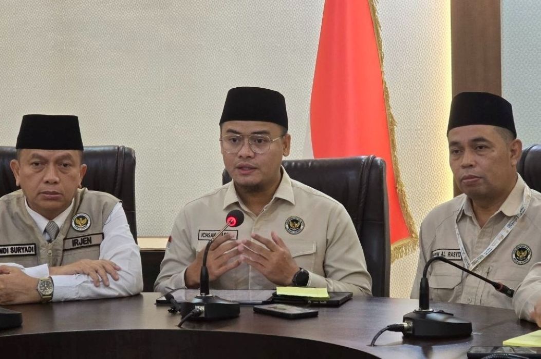 10fhaji catrawarta Three men in beige uniforms and black peci hats sit at a conference table during a formal briefing with an indonesian flag in the background and microphones in front of them