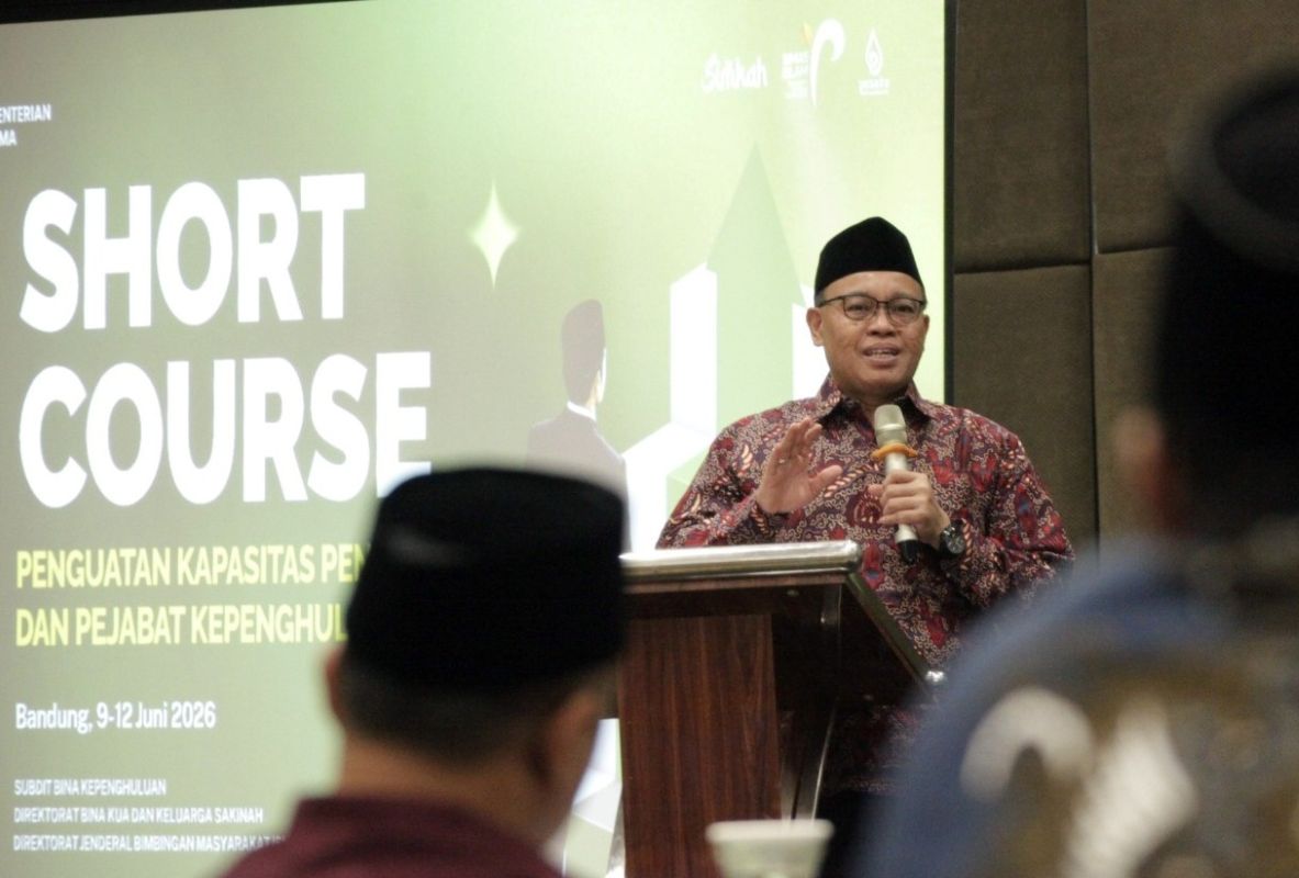 Man in batik shirt and black cap speaks at a podium during a seminar with a large short course banner behind