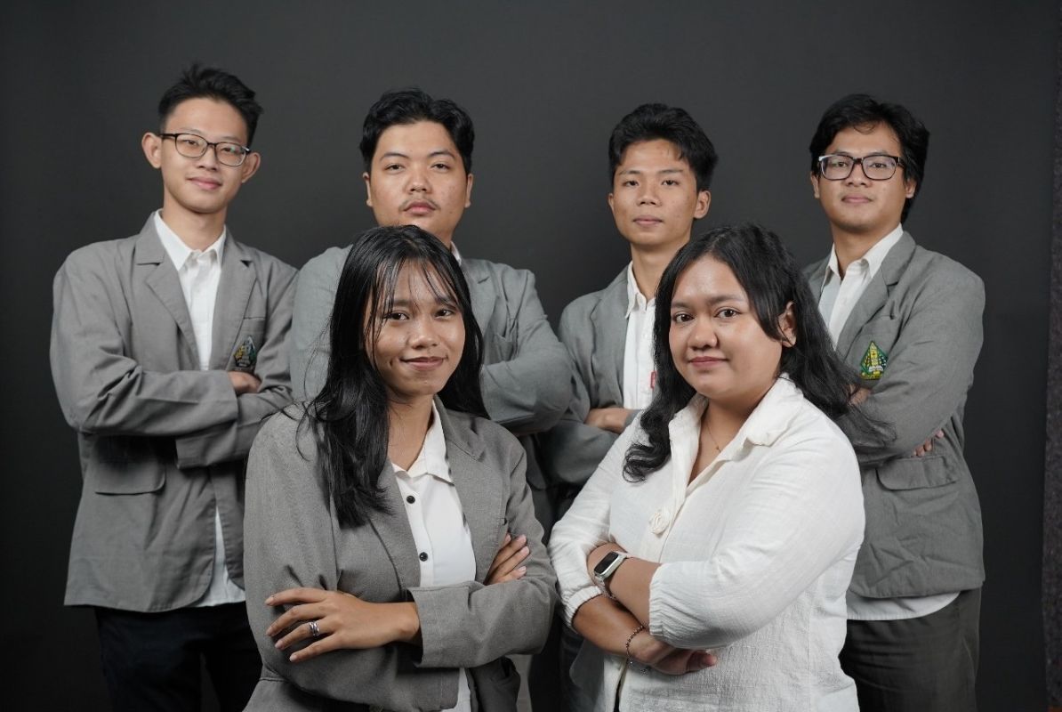 Group portrait of six professionals in gray blazers posing against a dark backdrop