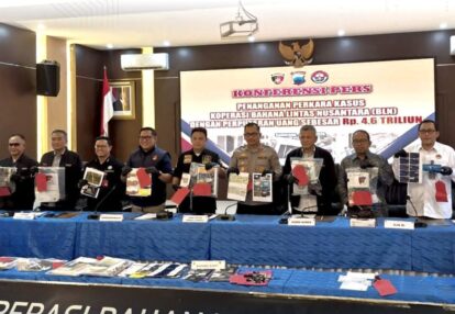 Indonesian officials stand behind a blue-draped table, displaying seized documents and evidence at a press conference with a large banner in the background.