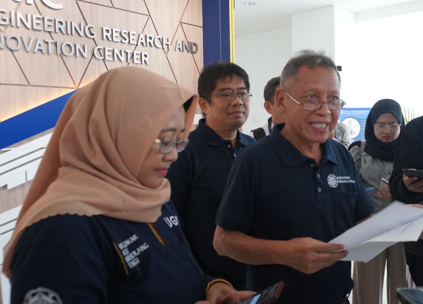 Group of professionals in navy shirts gathered indoors near a wall with engineering research and innovation center signage behind them