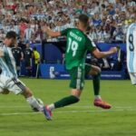 Soccer players from argentina blue and white stripes and a green clad opponent contest the ball on a crowded field during a match