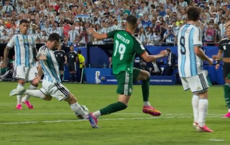 Soccer players from Argentina (blue-and-white stripes) and a green-clad opponent contest the ball on a crowded field during a match.