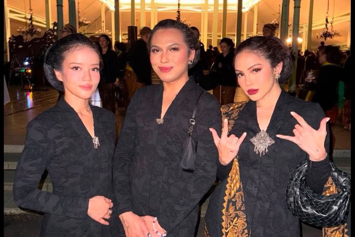 18flgbt catrawarta Three women in matching black patterned jackets posing together at an indoor evening event two with hands clasped in front and the rightmost making a rock on gesture with a black quilted bag at her side