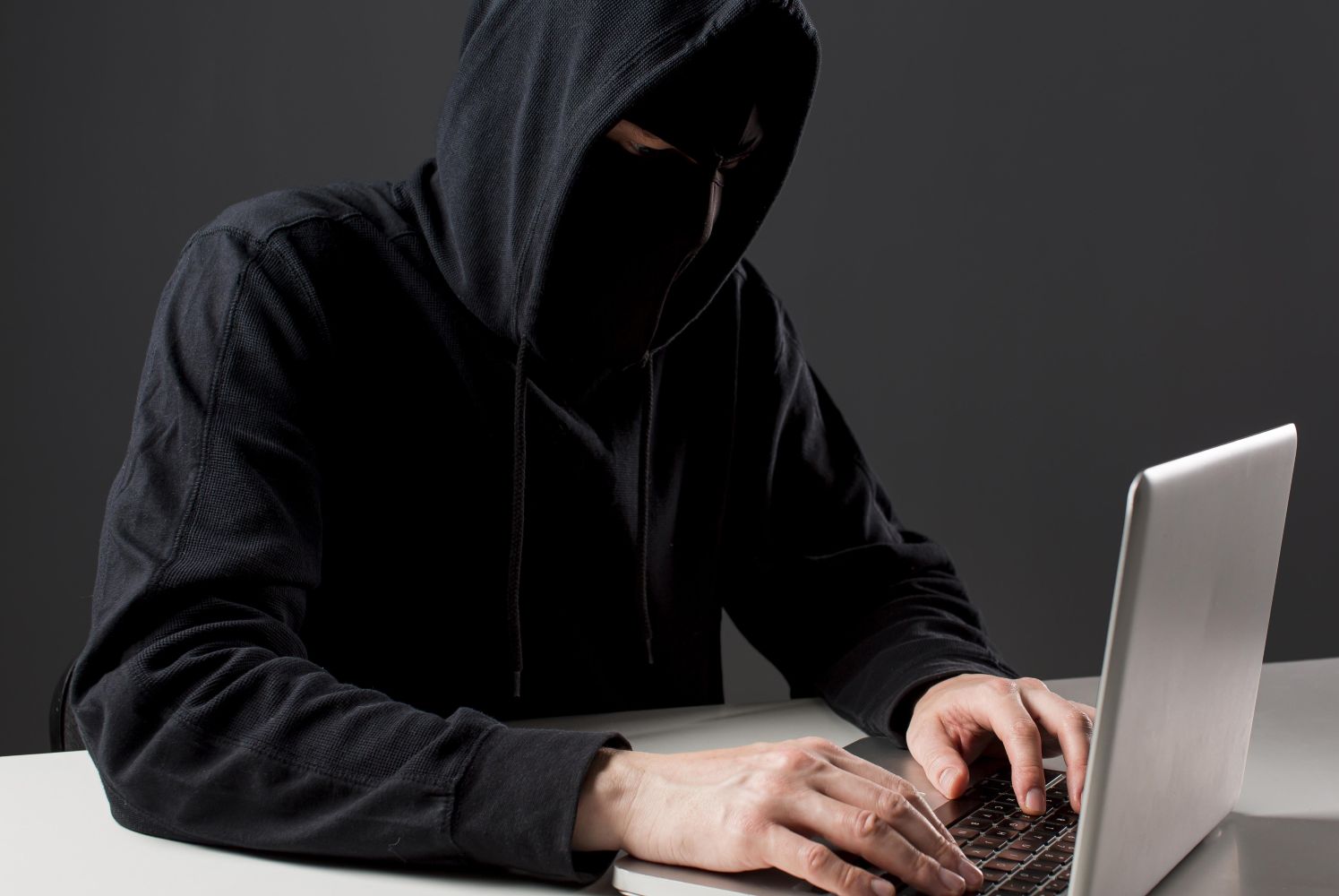 18ftipu catrawarta Person in a dark hoodie typing on a laptop face obscured by the hood in a dim setting