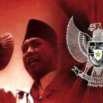 Man in a traditional cap speaks into a microphone with the indonesian garuda emblem in the red background behind him