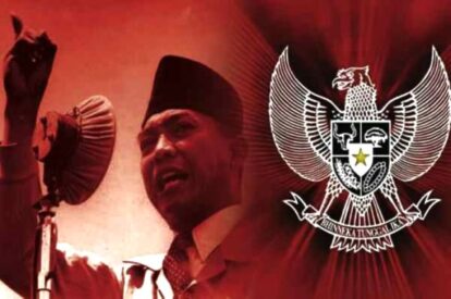 Man in a traditional cap speaks into a microphone with the indonesian garuda emblem in the red background behind him