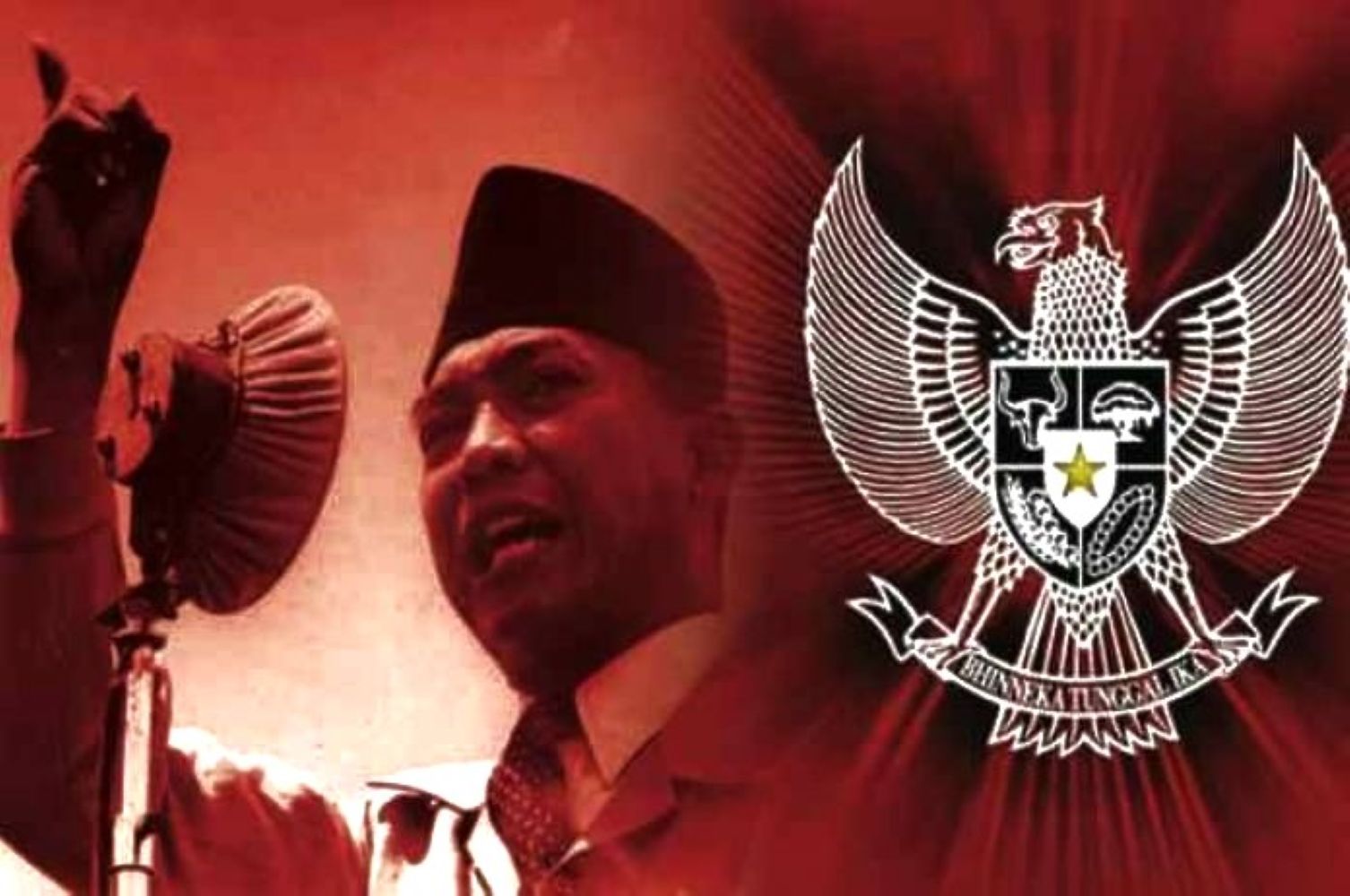 Man in a traditional cap speaks into a microphone with the indonesian garuda emblem in the red background behind him