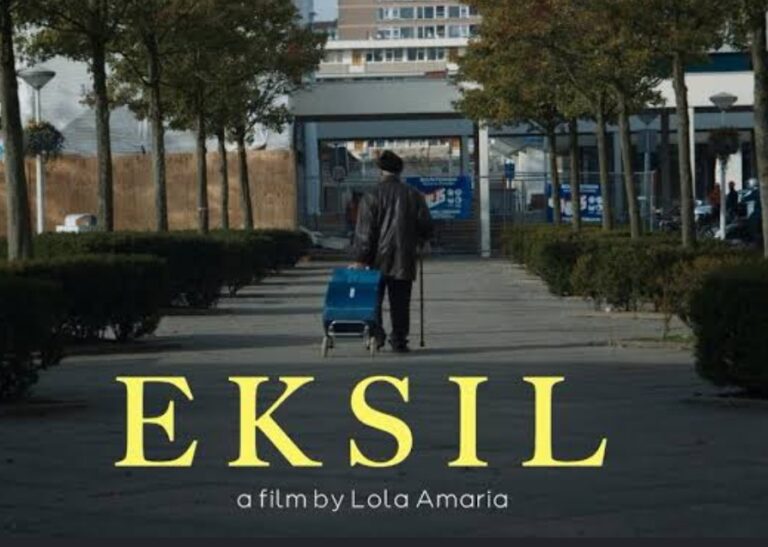 Poster for the film EKSIL by Lola Amaria, showing a person with a blue rolling cart walking down a walkway toward a building; large yellow title 'EKSIL' at the bottom with the subtitle 'a film by Lola Amaria'.