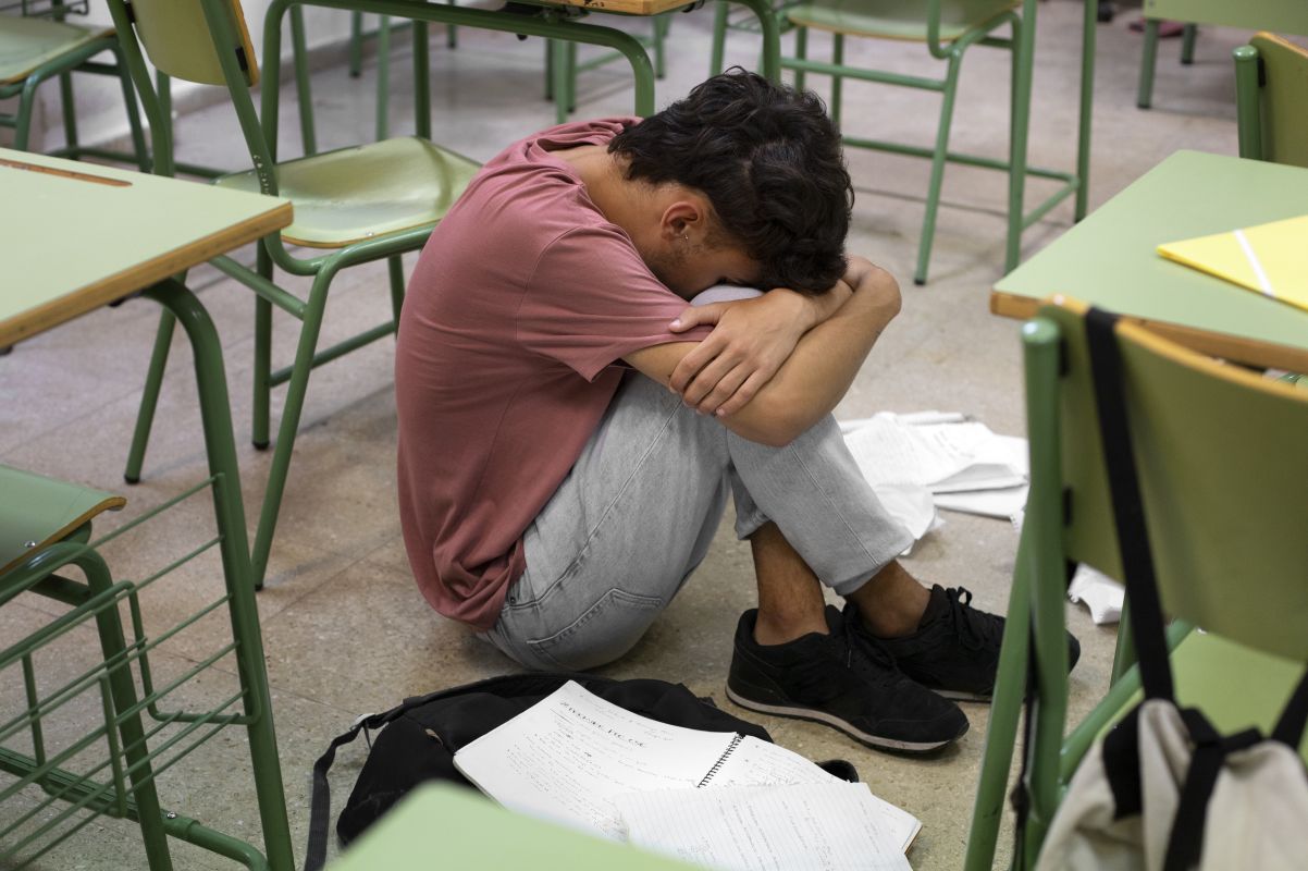 20fkorban catrawarta Student sitting on the classroom floor with head tucked into arms surrounded by desks and scattered papers