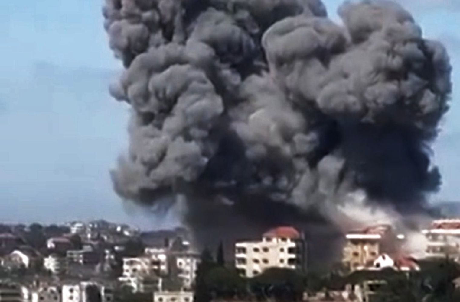 20fserangan catrawarta Massive plume of dark smoke rising from an explosion in a city with buildings in the foreground