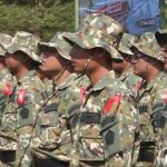 Line of soldiers in camouflage uniforms standing at attention with red ribbons on their chests under wide brim hats