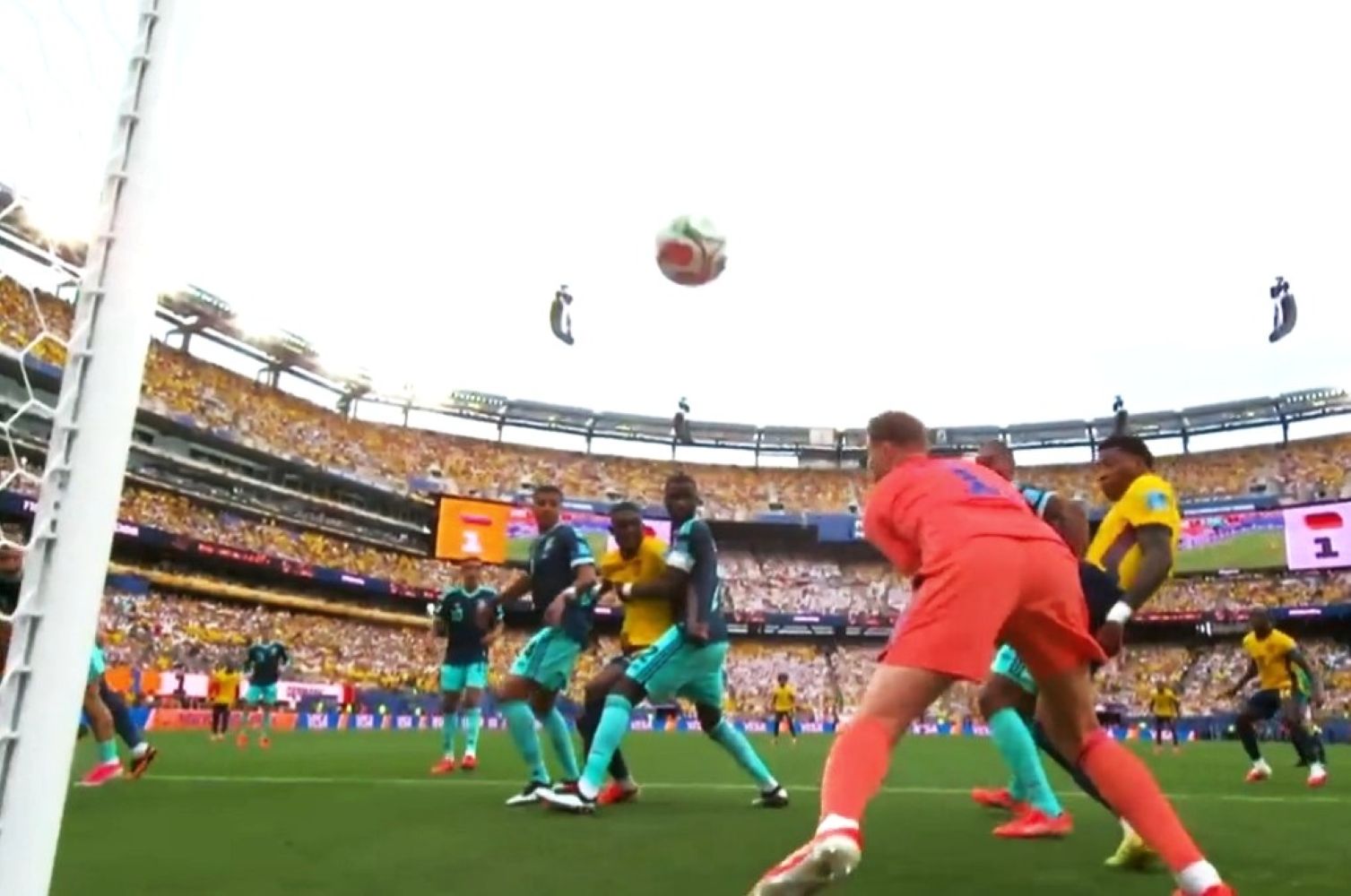 Soccer match near a goal as players in teal and yellow chase a ball in midair in a packed stadium