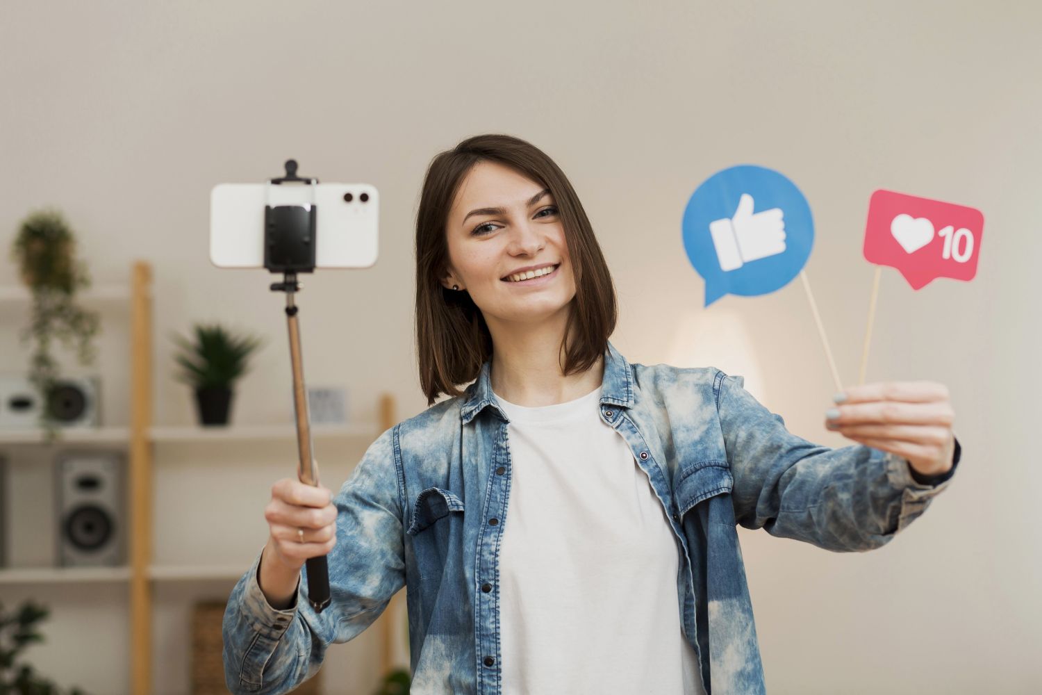 Smiling woman holds a selfie stick with a phone posing as social media like and heart icons appear beside her