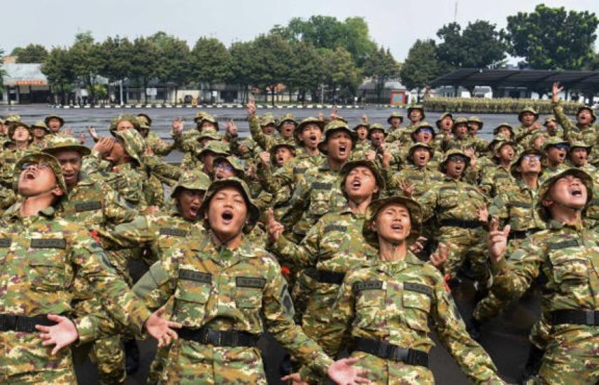 Large group of soldiers in camouflage uniforms outdoors many mouths open and arms raised as if cheering or shouting during a drill