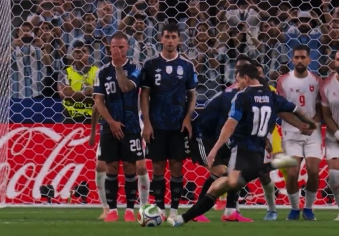 Soccer player in blue preparing to shoot a free kick as teammates form a wall in front of the goal
