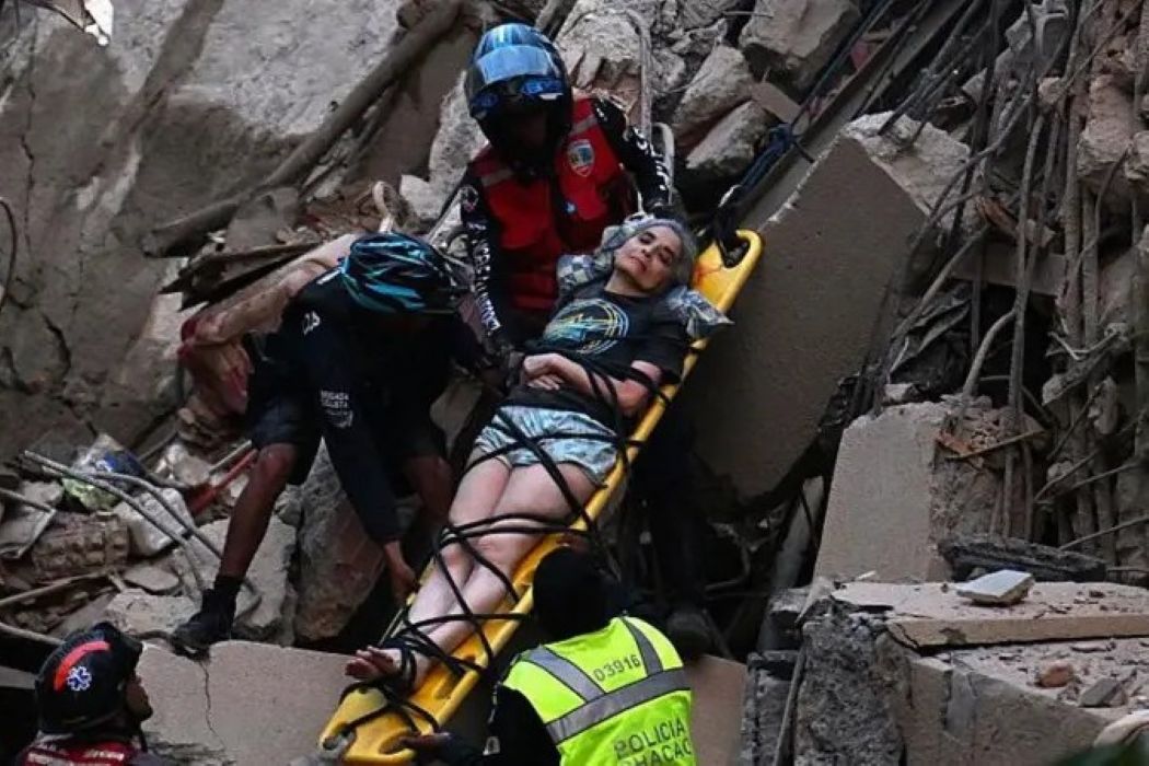 Rescuers carry an injured woman on a yellow stretcher through rubble after a collapse