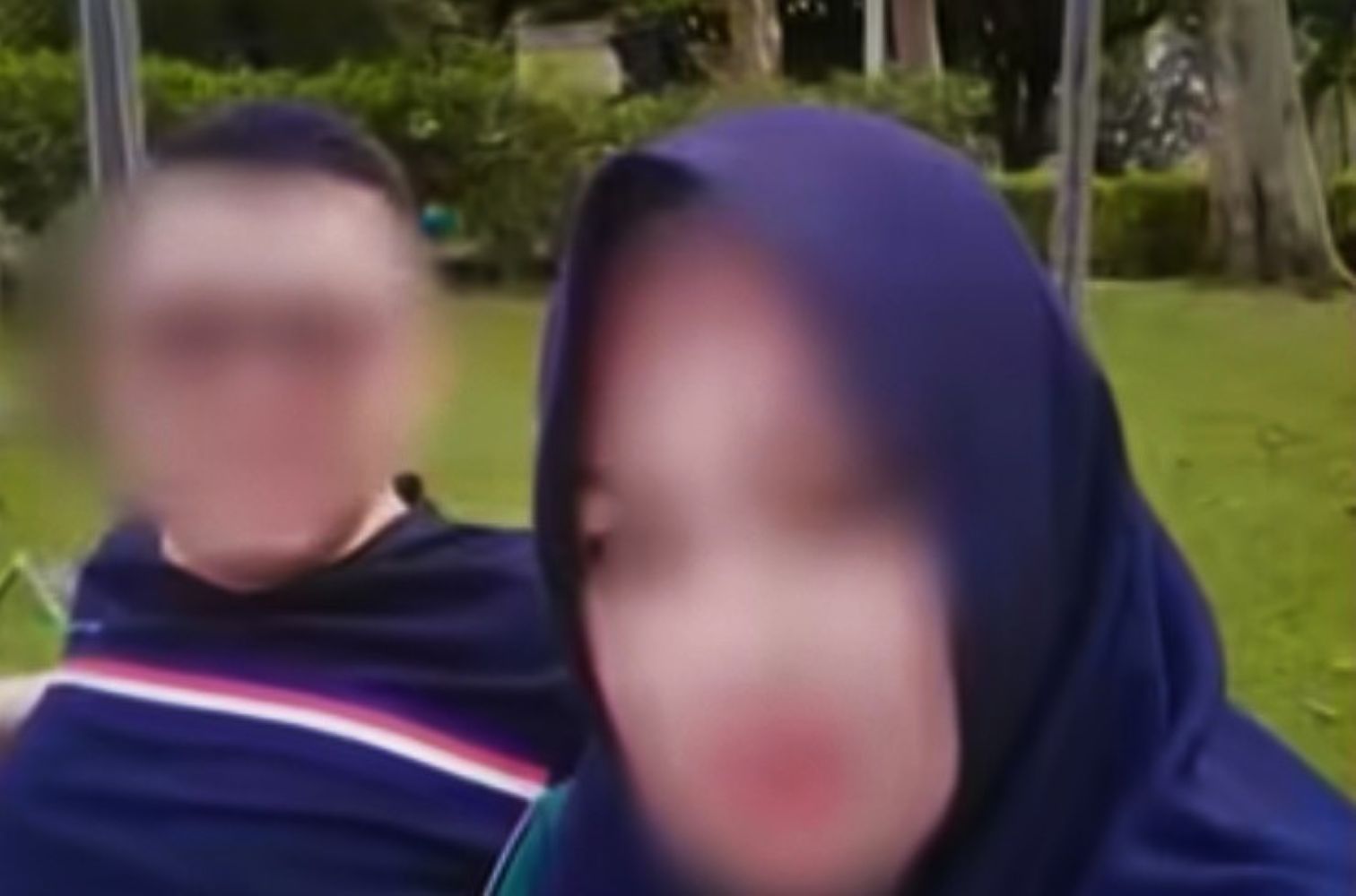 Two people sitting outdoors in a park a woman in a blue hijab is beside a man in a striped shirt their faces blurred
