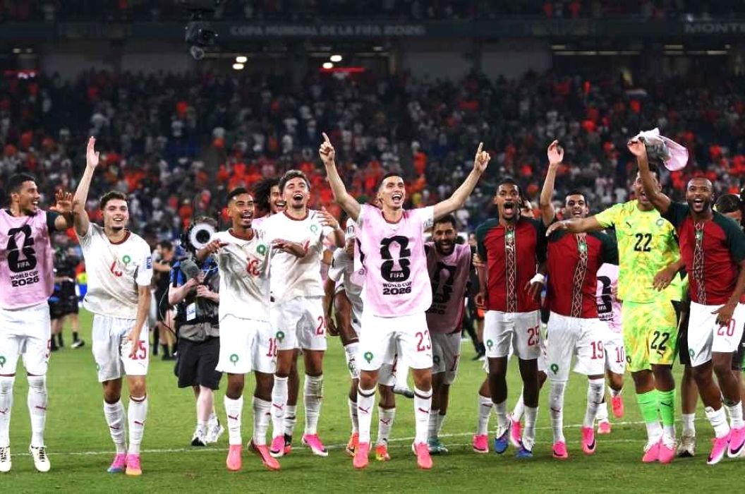 Soccer team celebrates on the field after a match players in white kits with pink bibs and a neonyellow goalkeeper crowd in the stands behind them