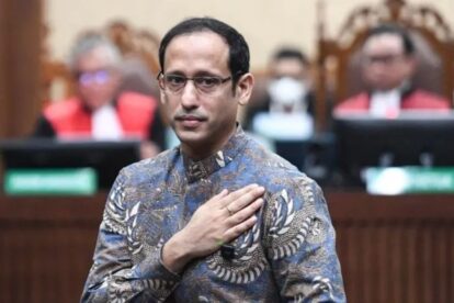 Man in a patterned batik shirt places his right hand over his heart during a formal oath-taking ceremony in a courtroom setting.