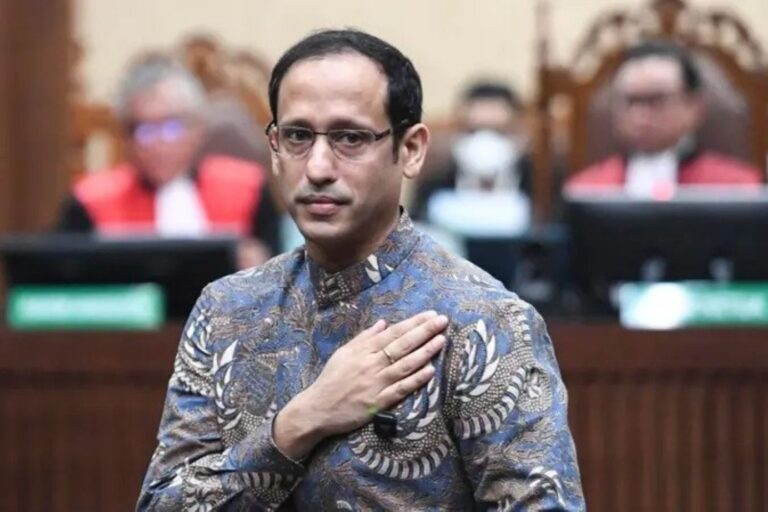 Man in a patterned batik shirt places his right hand over his heart during a formal oath-taking ceremony in a courtroom setting.