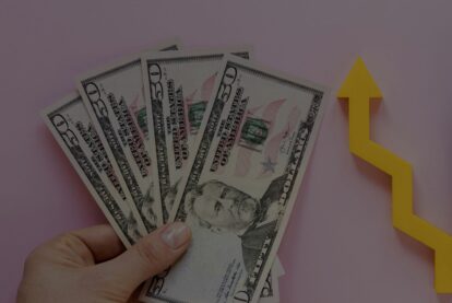 Fanned stack of $50 bills held in a hand with a yellow upward arrow symbolizing financial growth