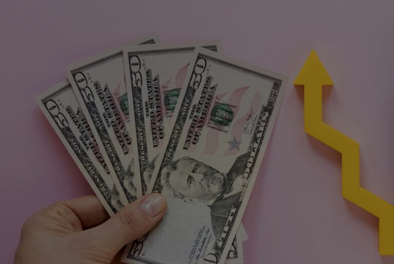Fanned stack of $50 bills held in a hand with a yellow upward arrow, symbolizing financial growth.