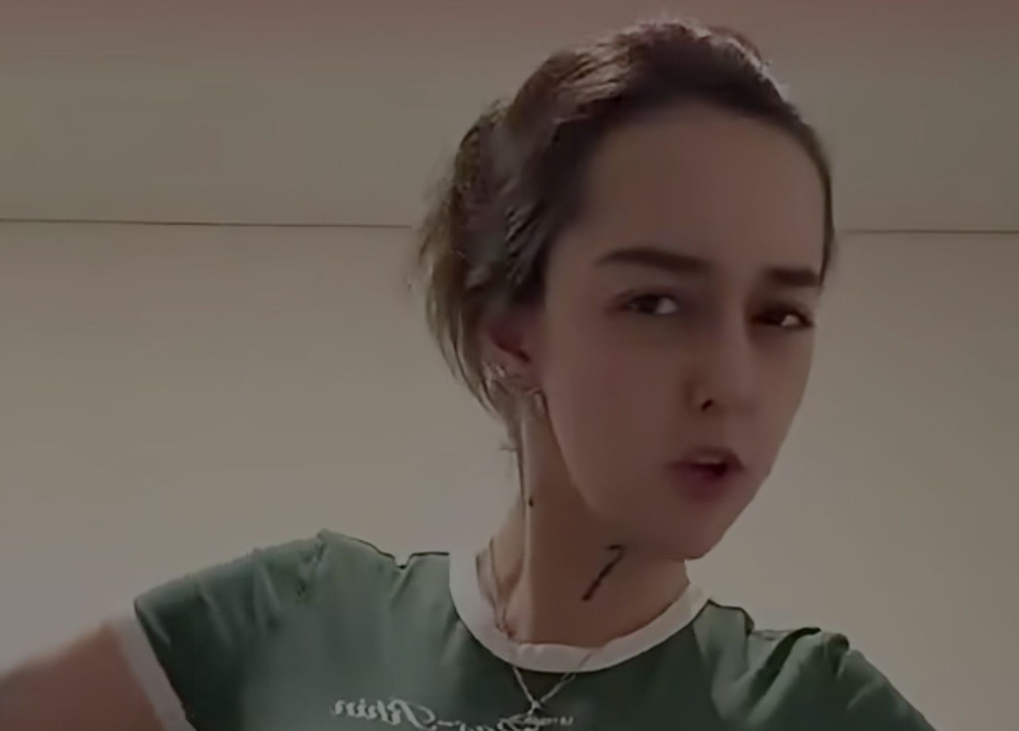 Close up of a person wearing a green shirt with a white collar looking at the camera indoors