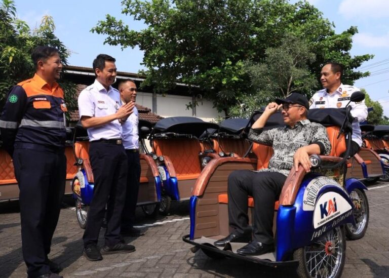 Man in a cap sits in a blue-and-orange pedicab while four uniformed men chat beside a row of orange rickshaws in a sunny parking lot.