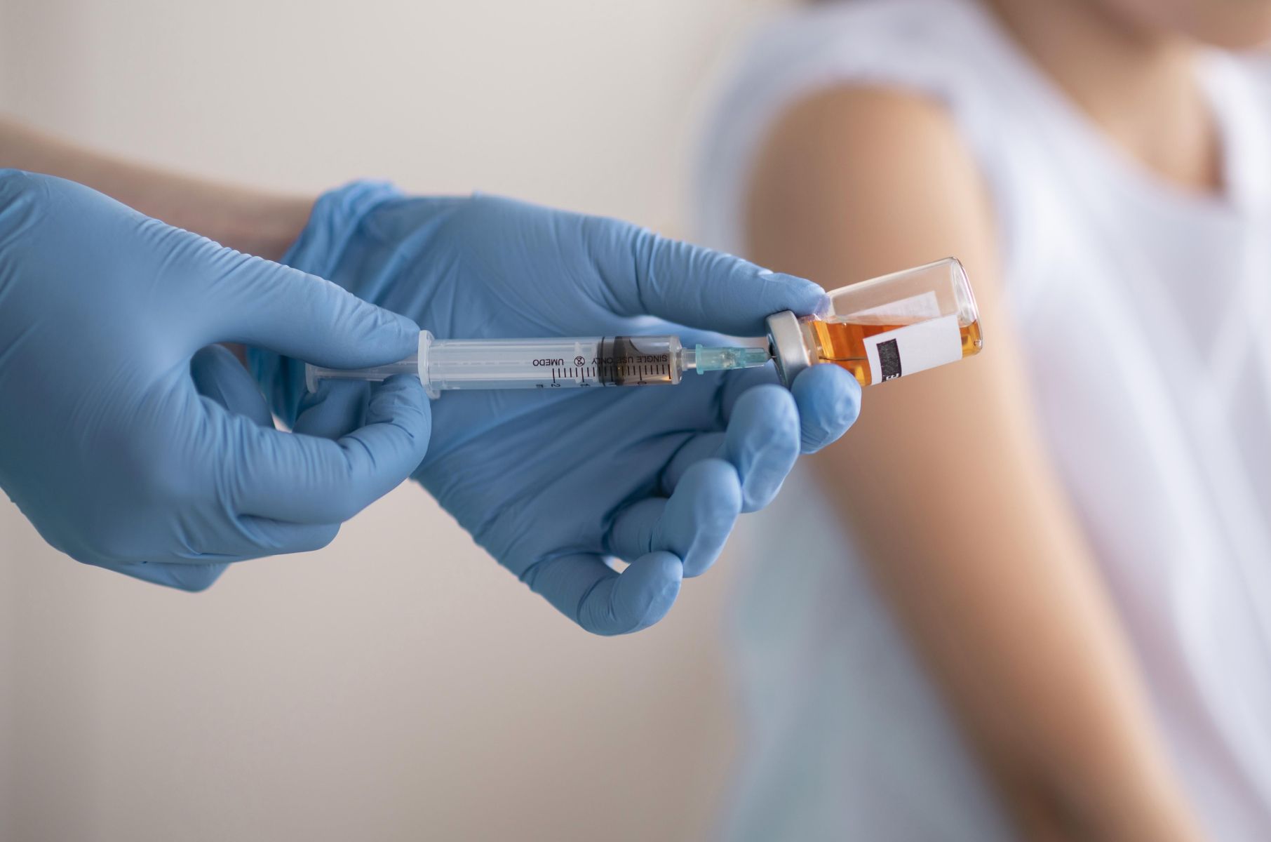 Medical worker in blue gloves draws vaccine from an amber vial into a syringe