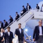 Group of men in dark blazers walking down stairs from a white airplane on the tarmac at the airport