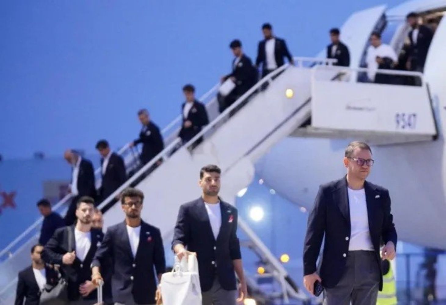 8firan1 catrawarta Group of men in dark blazers walking down stairs from a white airplane on the tarmac at the airport