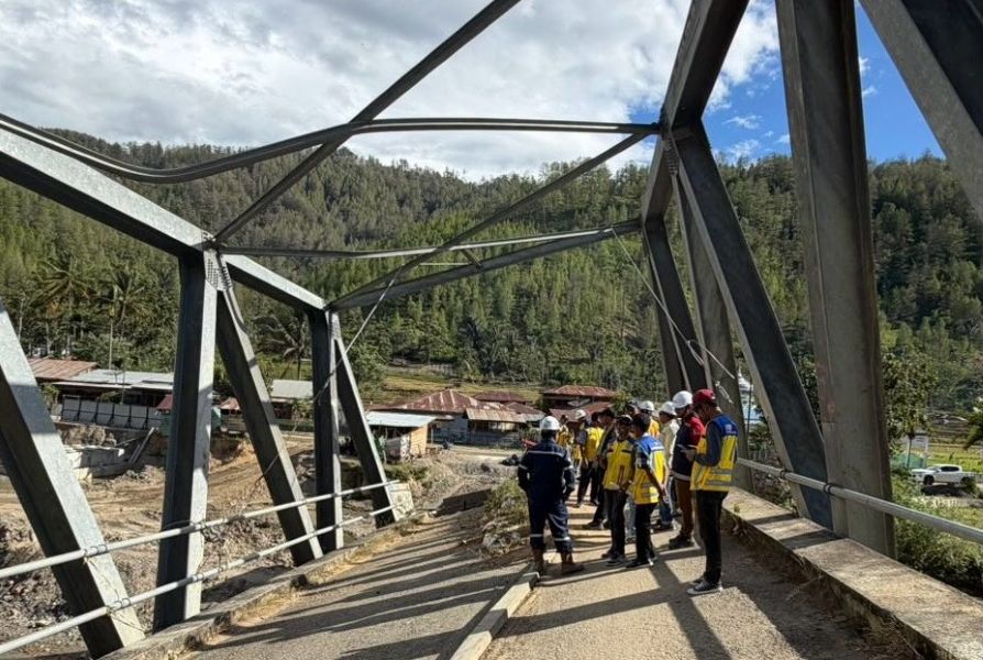 8fjembatan catrawarta Group of construction workers in hard hats and yellow vests stand on a partially completed steel bridge with a forested hillside in the background