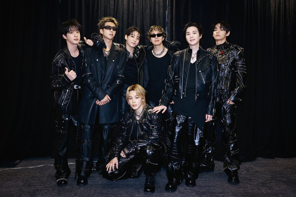 Bts catrawarta Seven men in black leather outfits posing together backstage against a dark curtain