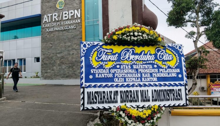 A government land office building atrbpn with a large blue condolence banner outside featuring floral decorations and indonesian text