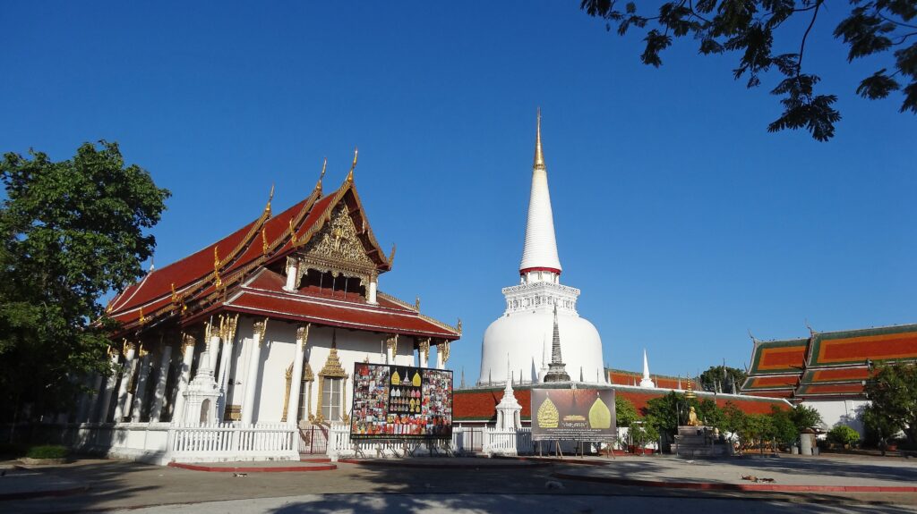 วัดพระมหาธาตุวรมหาวิหาร catrawarta Thai temple complex with a tall white stupa beside a ornate red roofed building under a clear blue sky