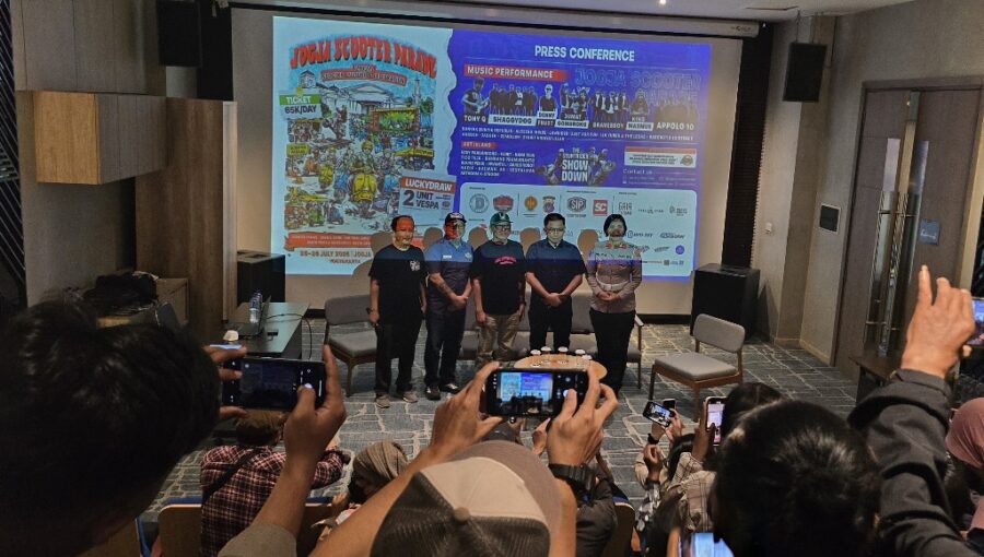 1002128509 catrawarta Group of five people standing on a stage in front of a large poster during a press conference audience taking photos in a conference room
