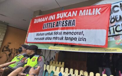 Large red banner in indonesian says rumah ini bukan milik little aresha with policesecurity officers in neon vests and onlookers nearby
