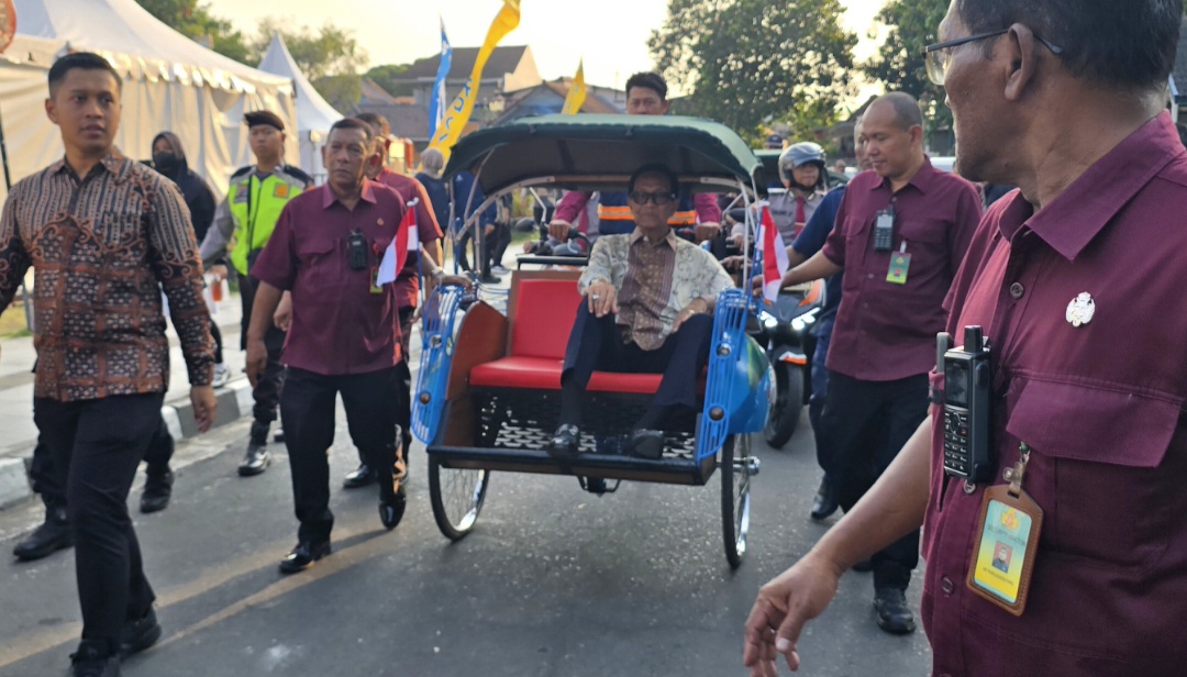 Gubernur diy sri sultan hb x catrawarta Man sits in a blue pedicab rickshaw with a red seat escorted by security guards at an outdoor event with tents and flags nearby