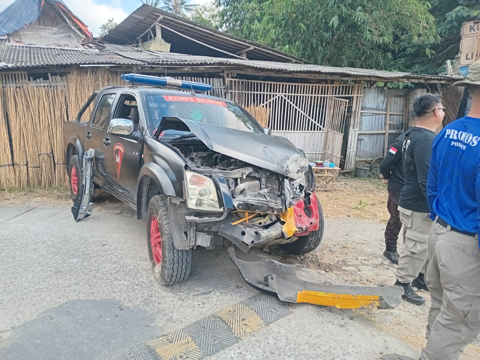 Mobil brimob polda diy terserempet ka bandara yia catrawarta Damaged black pickup truck with a crumpled front end and open hood blue emergency light on the roof two uniformed people stand nearby in a residential area