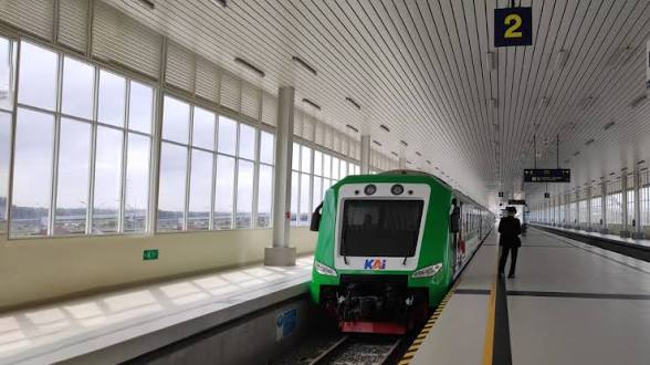 Kereta bandara yia dok Railink catrawarta Front view of a green commuter train stopped at platform 2 in a bright modern station with large windows a person stands on the platform nearby contrast